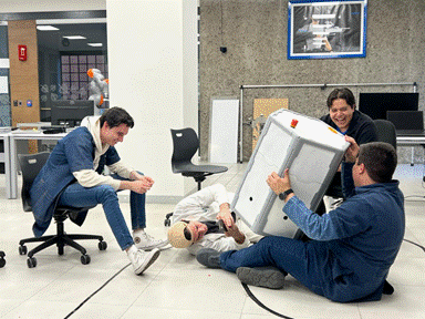 Several project participants gather around the RoboMeshA robot, lifting, inspecting, and testing the platform in a laboratory setting.