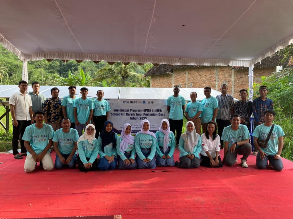 Group of EPICS in IEEE student and community participants posing together at a clean energy and water project event in Indonesia, with solar panels visible behind them.