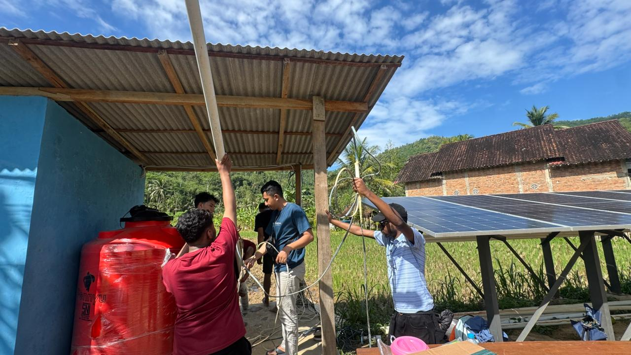 Project team members installing wiring and equipment beside solar panels and a water tank at the project site.