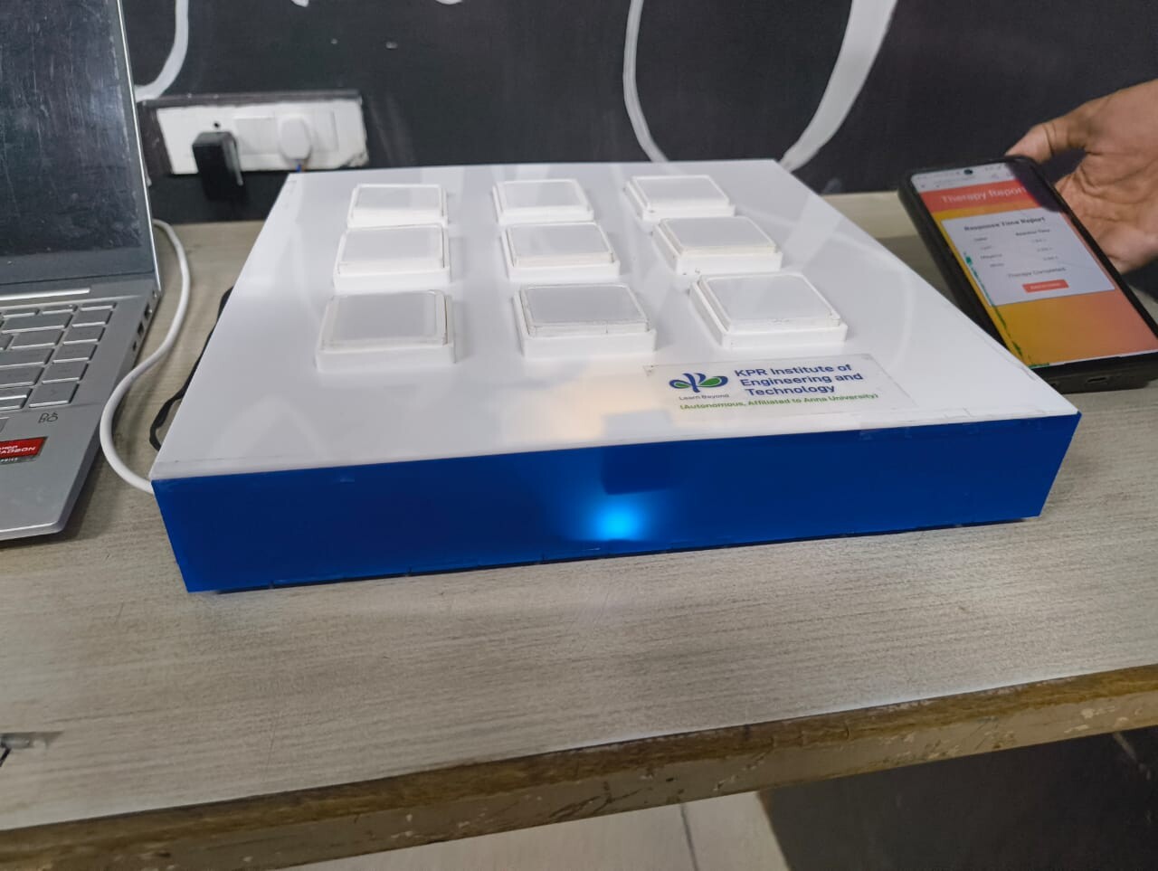 The NeuroGlow interactive rehabilitation system with a grid of nine square response panels beside a smartphone displaying a therapy report screen.